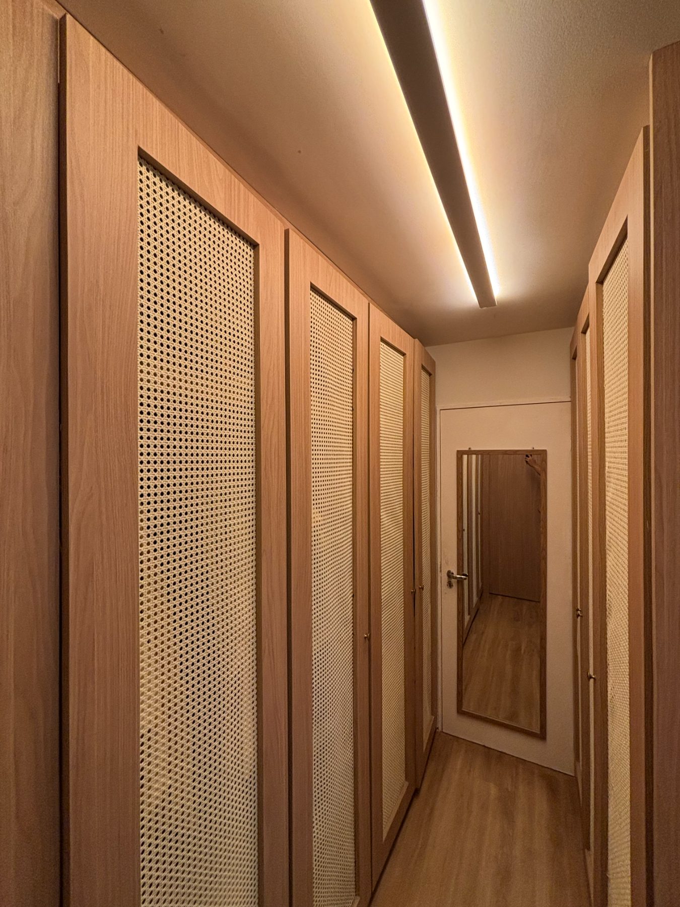 Corredor do closet com armários de palhinha dos dois lados e luminária linear no teto
