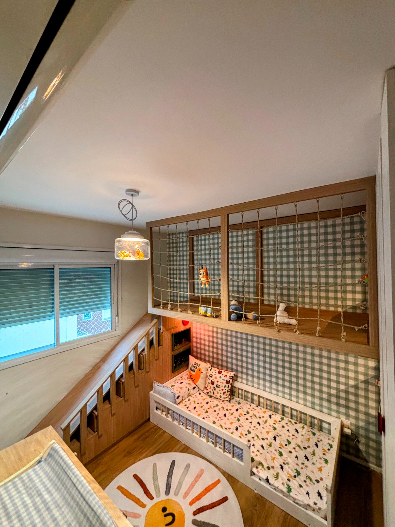 Quarto infantil visto de cima, com mezanino de rede, cama baixa e banco de guardar sob a janela